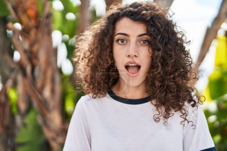 Photo for Hispanic woman with curly hair standing outdoors scared and amazed with open mouth for surprise, disbelief face - Royalty Free Image