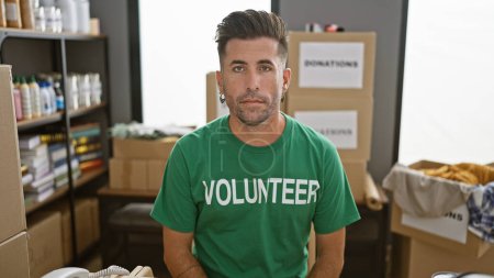 Téléchargez les photos : Jeune homme hispanique bénévole assis table avec un visage sérieux au centre de charité - en image libre de droit