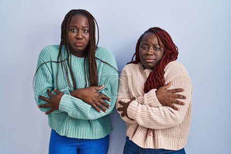 Photo for Two african woman standing over blue background shaking and freezing for winter cold with sad and shock expression on face - Royalty Free Image