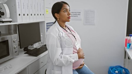 Téléchargez les photos : Attente jeune scientifique, femme hispanique sérieusement engagée dans la recherche, toucher le ventre enceinte au laboratoire - en image libre de droit