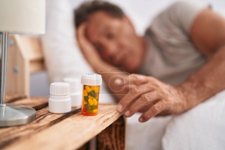 Téléchargez les photos : Moyen Age homme couché sur le lit tenant bouteille de pilules à la chambre - en image libre de droit