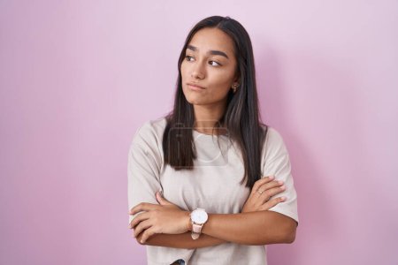 Téléchargez les photos : Young hispanic woman standing over pink background looking to the side with arms crossed convinced and confident - en image libre de droit