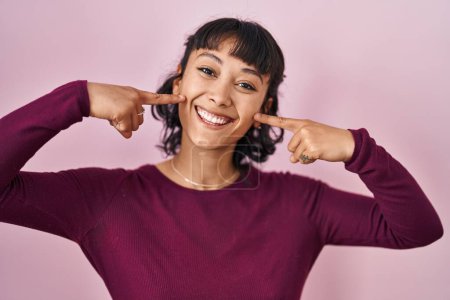 Téléchargez les photos : Young beautiful woman standing over pink background smiling cheerful showing and pointing with fingers teeth and mouth. dental health concept. - en image libre de droit