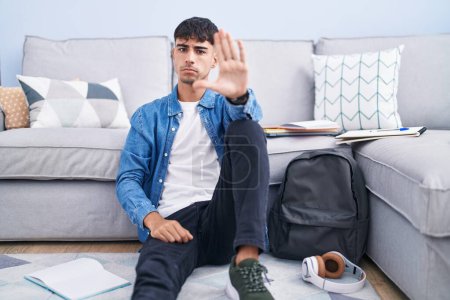 Photo for Young hispanic man sitting on the floor studying for university doing stop sing with palm of the hand. warning expression with negative and serious gesture on the face. - Royalty Free Image