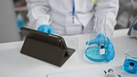 Téléchargez les photos : Les mains d'une femme scientifique mesurant habilement le liquide dans une éprouvette en laboratoire, s'engageant dans une recherche sérieuse avec un pavé tactile à sa disposition - en image libre de droit