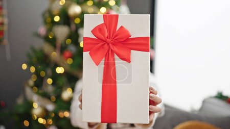 Photo for Young beautiful hispanic woman holding christmas gift over face at home - Royalty Free Image