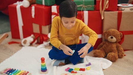 Foto de Adorable niño hispano jugando con las matemáticas juego sentado en el suelo por los regalos de Navidad en casa - Imagen libre de derechos