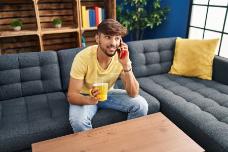 Photo for Young arab man drinking coffee and talking on the smartphone at home - Royalty Free Image