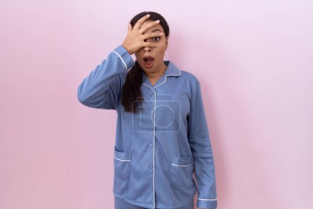 Photo for Young arab woman wearing blue pajama peeking in shock covering face and eyes with hand, looking through fingers with embarrassed expression. - Royalty Free Image