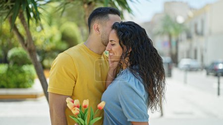 Téléchargez les photos : Homme et femme couple surprise avec bouquet de fleurs baisers au parc - en image libre de droit
