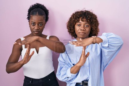 Photo for Two african women standing over pink background doing time out gesture with hands, frustrated and serious face - Royalty Free Image