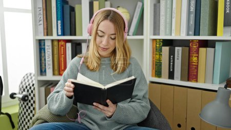 Téléchargez les photos : Jeune étudiante blonde écoutant un livre de lecture de musique à la bibliothèque de l'université - en image libre de droit