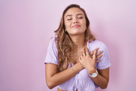 Photo for Young hispanic woman standing over pink background smiling with hands on chest with closed eyes and grateful gesture on face. health concept. - Royalty Free Image