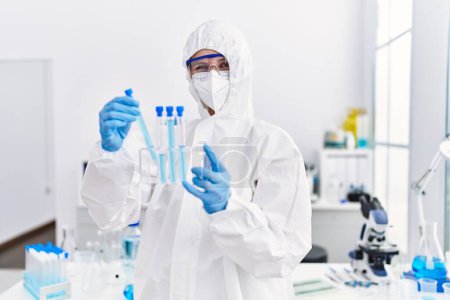 Téléchargez les photos : Jeune scientifique blonde portant un uniforme de sécurité tenant des éprouvettes au laboratoire - en image libre de droit