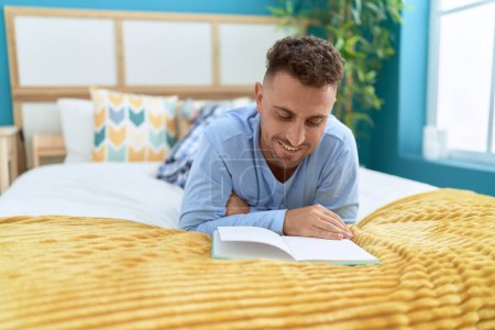 Téléchargez les photos : Jeune homme hispanique lecture livre couché sur le lit dans la chambre - en image libre de droit