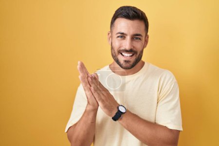 Photo for Handsome hispanic man standing over yellow background clapping and applauding happy and joyful, smiling proud hands together - Royalty Free Image