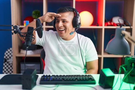 Photo for Young hispanic man playing video games very happy and smiling looking far away with hand over head. searching concept. - Royalty Free Image
