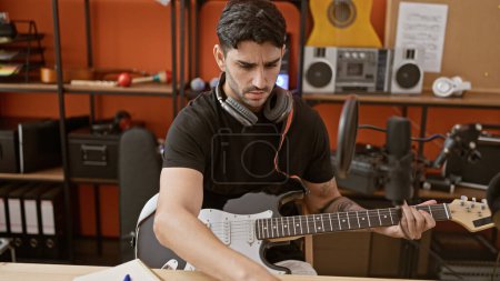 Téléchargez les photos : Jeune homme hispanique musicien jouant de la guitare électrique composer chanson au studio de musique - en image libre de droit