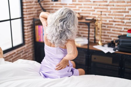 Foto de Mujer de pelo gris de mediana edad que sufre una lesión en la espalda sentada en la cama en el dormitorio - Imagen libre de derechos