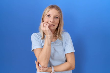 Foto de Mujer caucásica joven que usa una camiseta azul casual que se ve estresada y nerviosa con las manos en las uñas mordedoras de la boca. problema de ansiedad. - Imagen libre de derechos