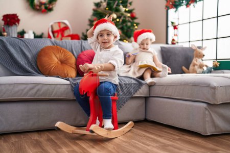 Téléchargez les photos : Deux enfants jouent avec des rennes berçant et dessinant sur ordinateur portable par arbre de Noël à la maison - en image libre de droit