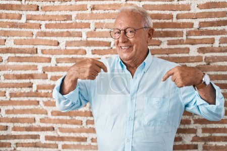 Photo for Senior man with grey hair standing over bricks wall looking confident with smile on face, pointing oneself with fingers proud and happy. - Royalty Free Image