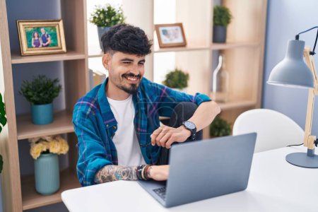 Téléchargez les photos : Jeune homme hispanique utilisant un ordinateur portable assis sur la table à la maison - en image libre de droit