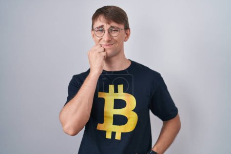 Photo for Caucasian blond man wearing bitcoin t shirt looking stressed and nervous with hands on mouth biting nails. anxiety problem. - Royalty Free Image