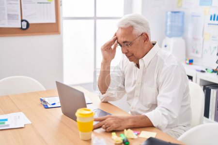 Foto de Hombre de pelo gris de mediana edad trabajador de negocios estresado utilizando el ordenador portátil en la oficina - Imagen libre de derechos