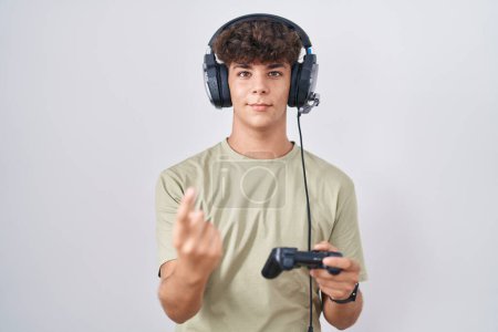 Téléchargez les photos : Adolescent hispanique jouant contrôleur de tenue de jeu vidéo appel viennent ici geste avec la main invitant accueillant heureux et souriant - en image libre de droit