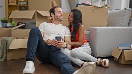 Foto de Hermosa pareja sentada en el suelo juntos usando un teléfono inteligente sonriendo en un nuevo hogar - Imagen libre de derechos