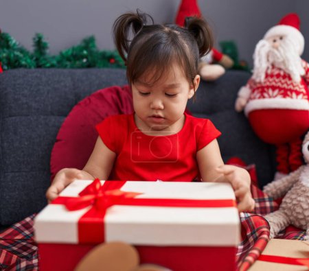 Foto de Adorable chica china sosteniendo regalo sentado en el sofá por la decoración de Navidad en casa - Imagen libre de derechos