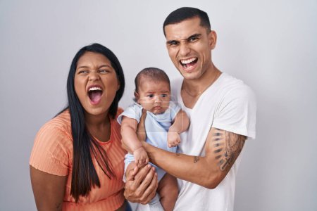 Photo for Young hispanic couple with baby standing together over isolated background angry and mad screaming frustrated and furious, shouting with anger. rage and aggressive concept. - Royalty Free Image