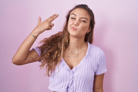 Téléchargez les photos : Young hispanic woman standing over pink background shooting and killing oneself pointing hand and fingers to head like gun, suicide gesture. - en image libre de droit