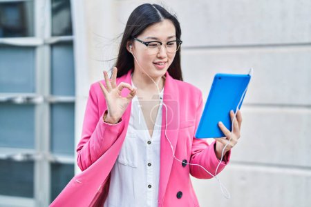 Foto de Mujer joven china usando touchpad usando auriculares haciendo signo ok con los dedos, sonriendo gesto amistoso excelente símbolo - Imagen libre de derechos