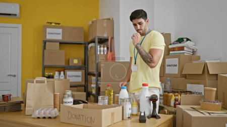 Téléchargez les photos : Jeune homme hispanique bénévole mettant des produits sur la boîte en carton de don au centre de charité - en image libre de droit