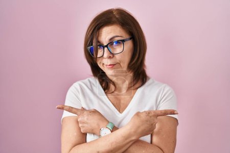 Photo for Middle age hispanic woman standing over pink background pointing to both sides with fingers, different direction disagree - Royalty Free Image