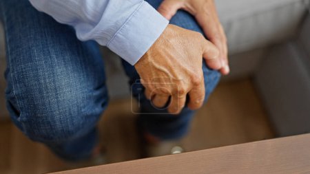 Téléchargez les photos : Moyen Age femme hispanique assis sur le canapé souffrant de blessure au genou à la maison - en image libre de droit