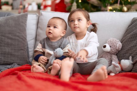 Foto de Brother and sister sitting on sofa by christmas tree at home - Imagen libre de derechos