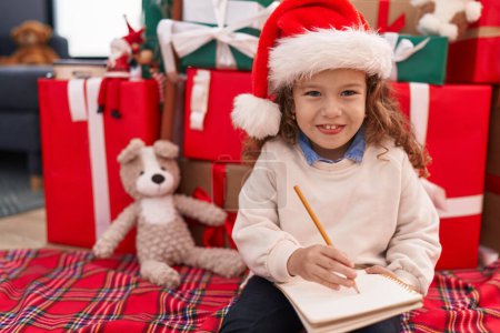 Foto de Adorable rubio niño escribiendo santa claus carta sentado en el suelo por regalos de Navidad en casa - Imagen libre de derechos