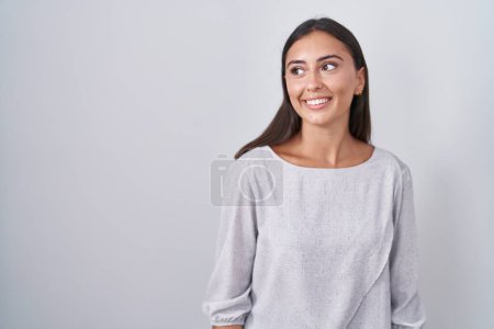Téléchargez les photos : Young hispanic woman standing over white background looking away to side with smile on face, natural expression. laughing confident. - en image libre de droit