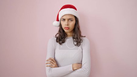 Photo for Young beautiful hispanic woman standing upset wearing christmas hat over isolated pink background - Royalty Free Image