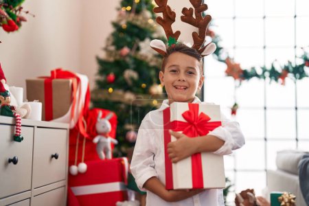 Foto de Adorable niño hispano sosteniendo regalo de Navidad de pie en casa - Imagen libre de derechos