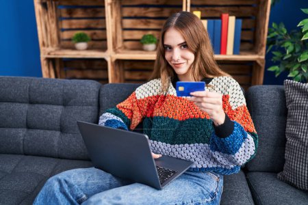 Foto de Mujer joven usando portátil y tarjeta de crédito sentado en el sofá en casa - Imagen libre de derechos