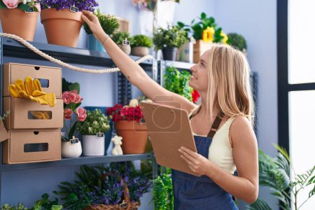 Photo for Young blonde woman florist smiling confident organize shelving at florist store - Royalty Free Image