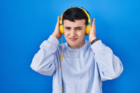Téléchargez les photos : Personne non binaire écoutant de la musique à l'aide d'écouteurs couvrant les oreilles avec des doigts avec une expression agacée pour le bruit de la musique forte. concept sourd. - en image libre de droit