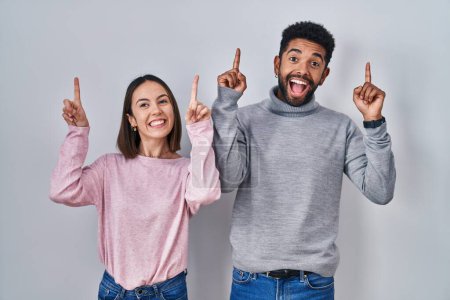 Photo for Young hispanic couple standing together smiling amazed and surprised and pointing up with fingers and raised arms. - Royalty Free Image