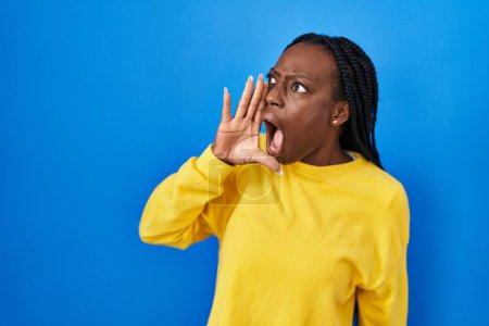 Photo for Beautiful black woman standing over blue background shouting and screaming loud to side with hand on mouth. communication concept. - Royalty Free Image