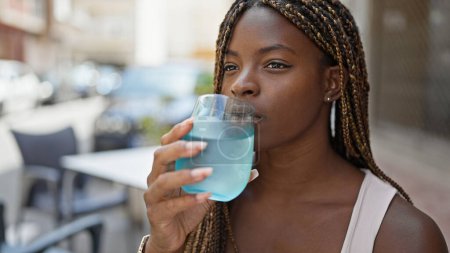 Téléchargez les photos : Femme afro-américaine buvant un verre d'eau assis sur la table à la terrasse du café - en image libre de droit
