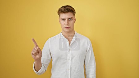Photo for Young caucasian man saying no with finger and serious face over isolated yellow background - Royalty Free Image